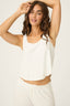 Woman wearing a white sleeveless top and pants on a plain background